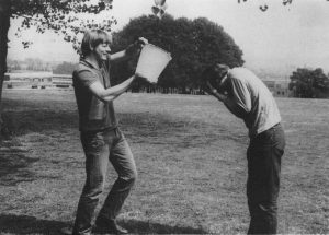 Monochrome photograph of two students, one about to pour a bucket of water over the other.