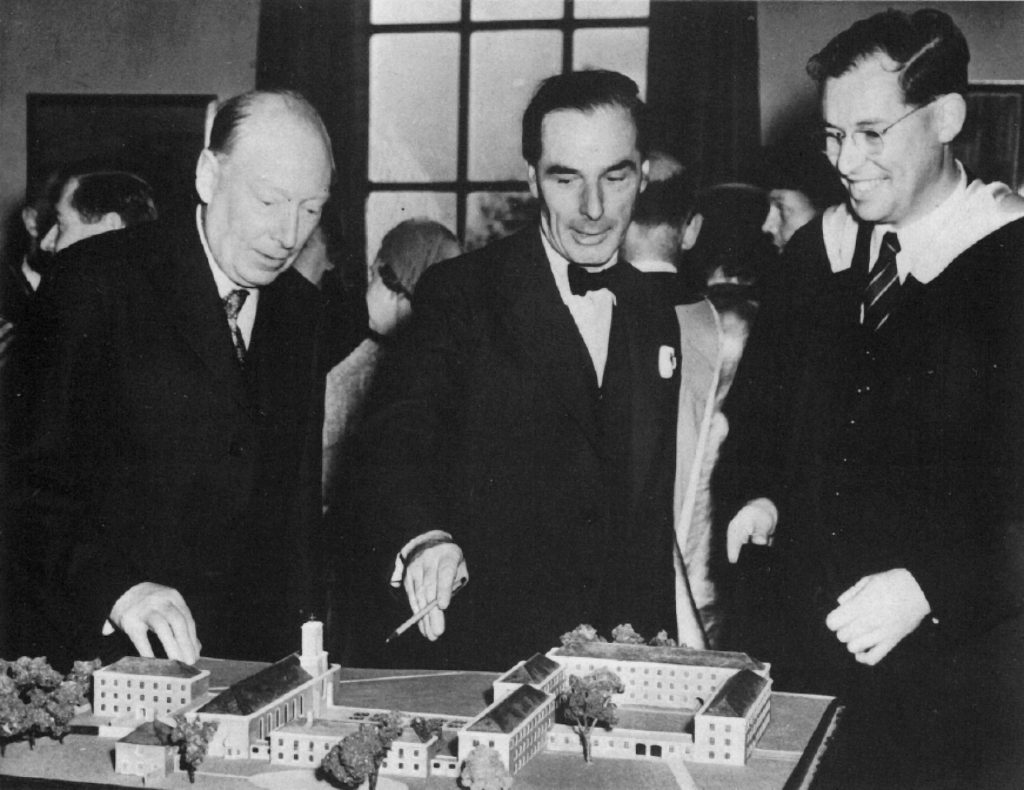 A monochrome photograph of Mr D. H. McMorran, with Mr. C. T. Cripps and his son Mr. C. H. Cripps look at a scale model of Cripps Hall following its opening.